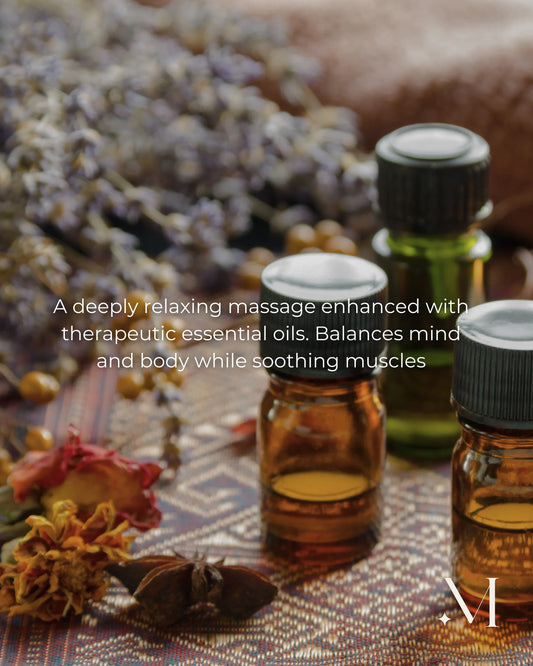 Aromatherapie massageflesjes met essentiële oliën en gedroogde bloemen op een spa-achtig doekje.