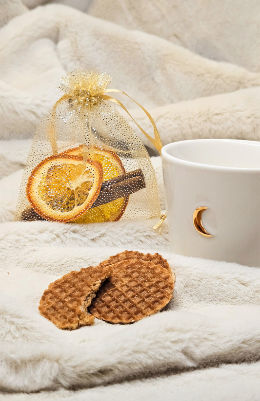 White mug with gold crescent, stroopwafels, dried orange slices, on soft blanket